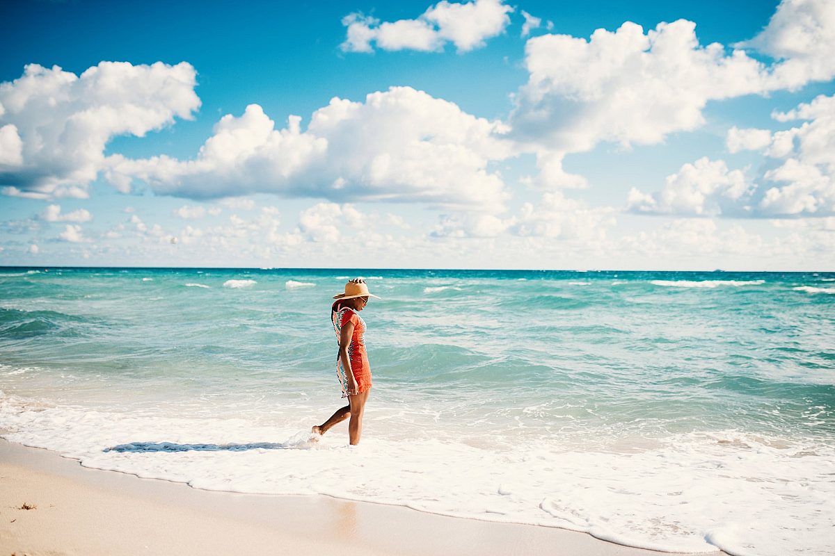 woman wearing a straw hat walking in the side of the blue beach with wide sky view